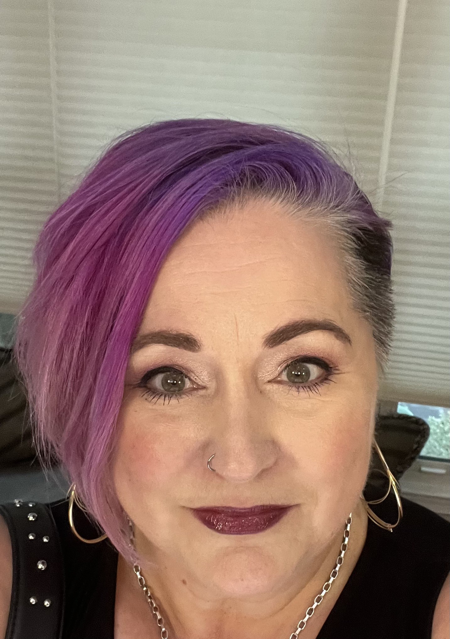 6d0f2f28-b548-43d8-9404-df4effc47c54 - Star Point Counseling Close-up of a woman with short purple hair, green eyes, and dark lipstick, wearing hoop earrings and a nose ring against a background of blinds.